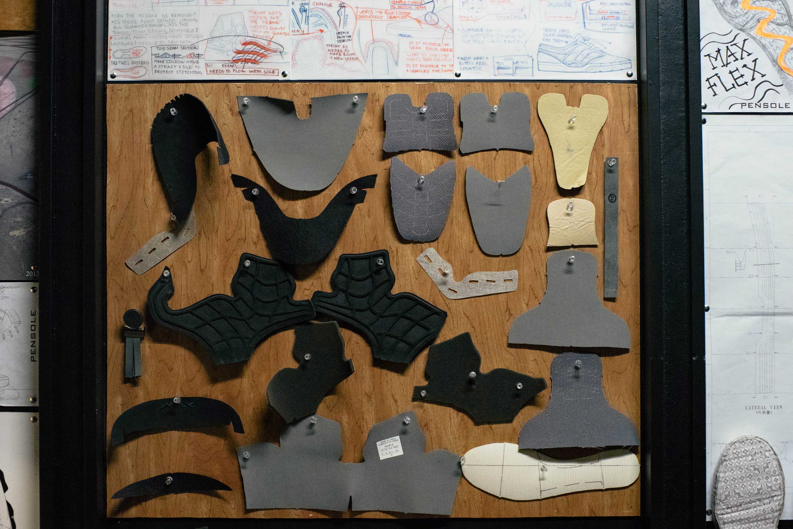 Multiple shoe design pieces pinned up on a wooden board.