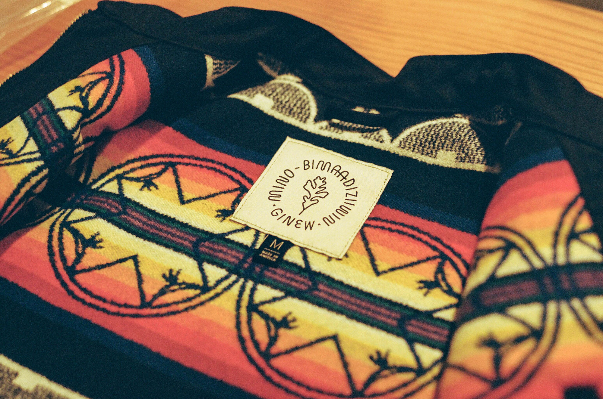 The inside of the top of a black Ginew jacket. Inside is lined with designs, patterns, and symbols that reflect the Native American community.