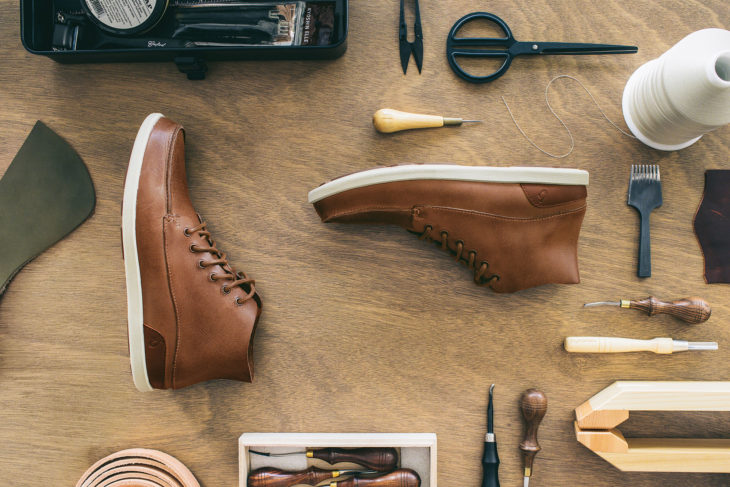 Handcrafted OluKai shoes, supple brown leather with white base, surrounded by the tools used to construct them.
