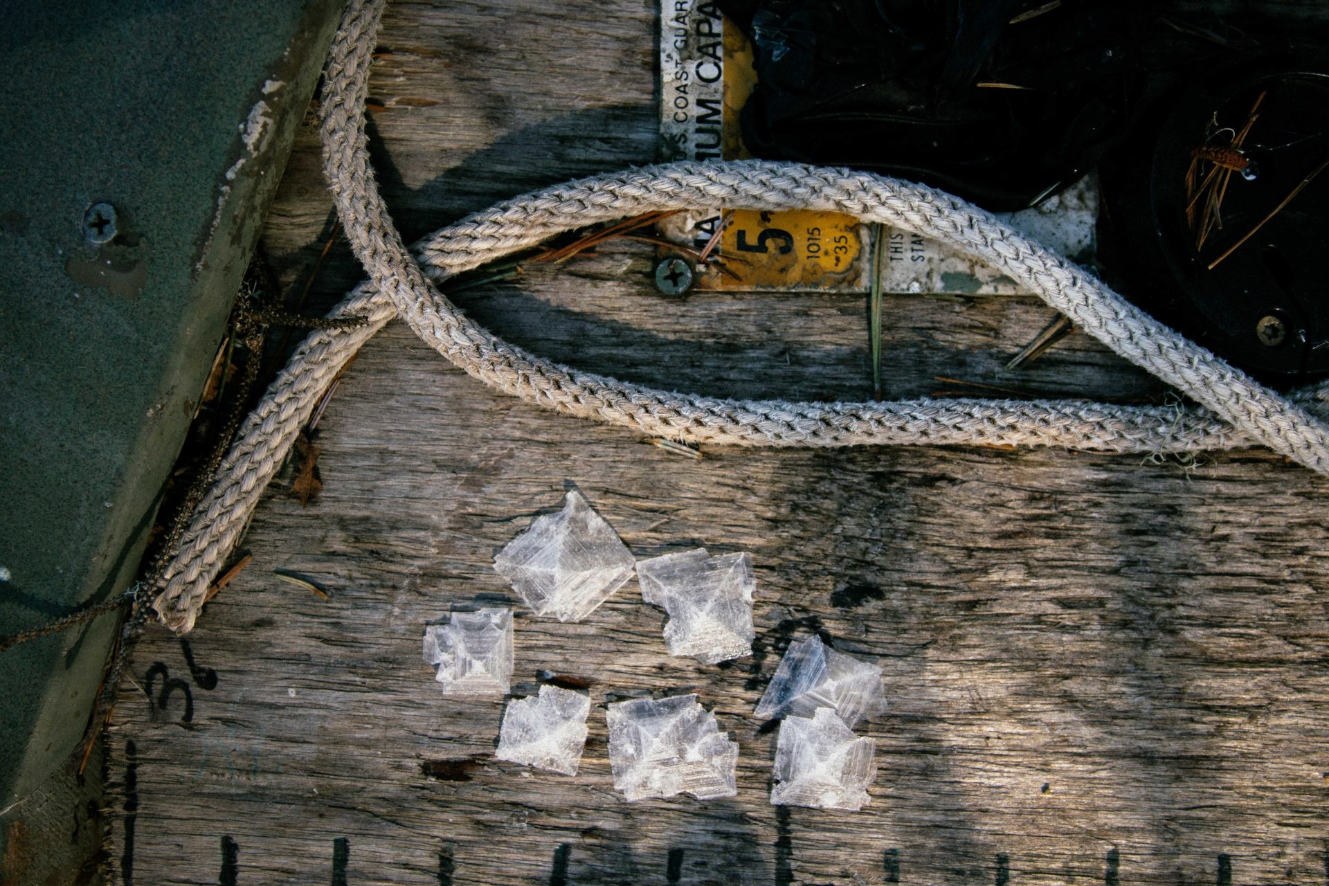 Paper like slices of salt lay on the deck of a boat, just below a rope.