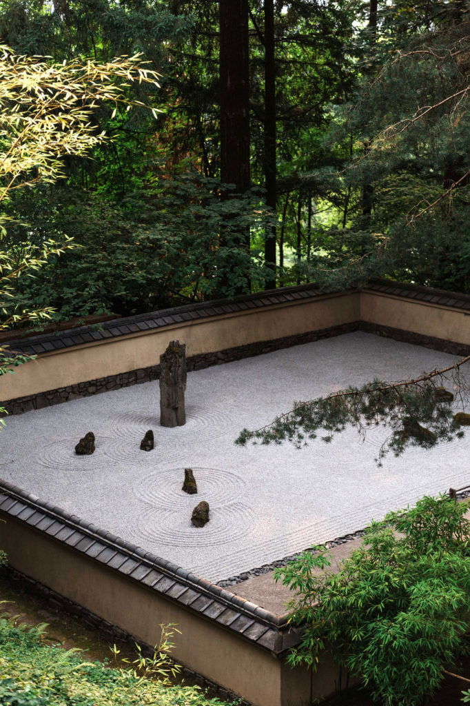 A Japanese rock garden with 4 small rocks and a larger rock standing tall behind them.