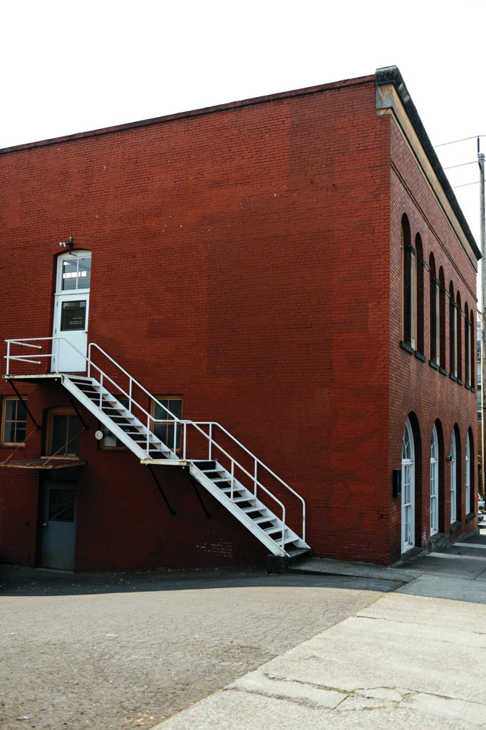 White stairs and a small white door alongside a red brick building that leads into a print studio.