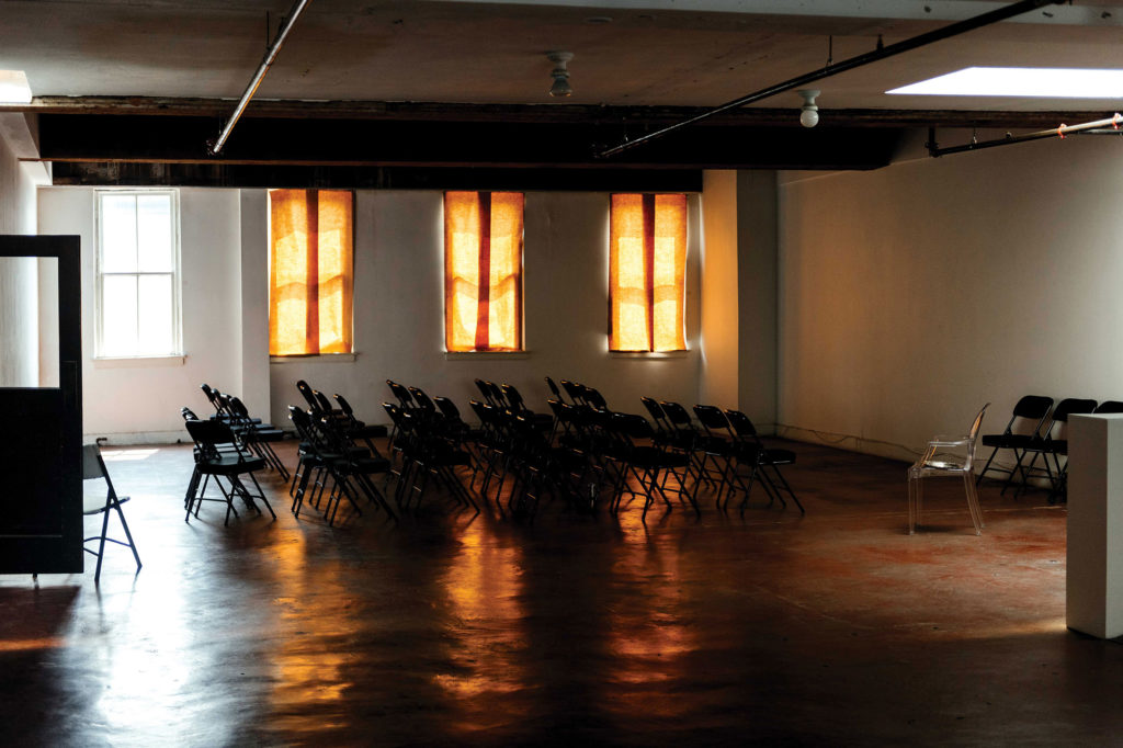 A dimly lit room with the center of it darken by curtains and filled with rows of chairs.