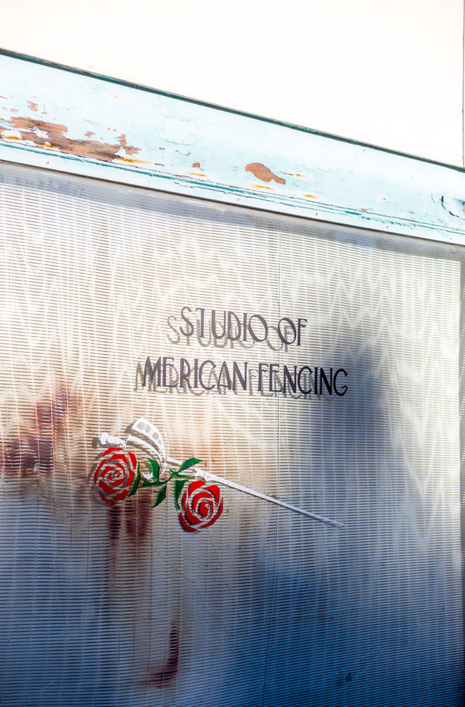 A rusted sign that reads "Studio of American Fencing" along with a depiction of a rose