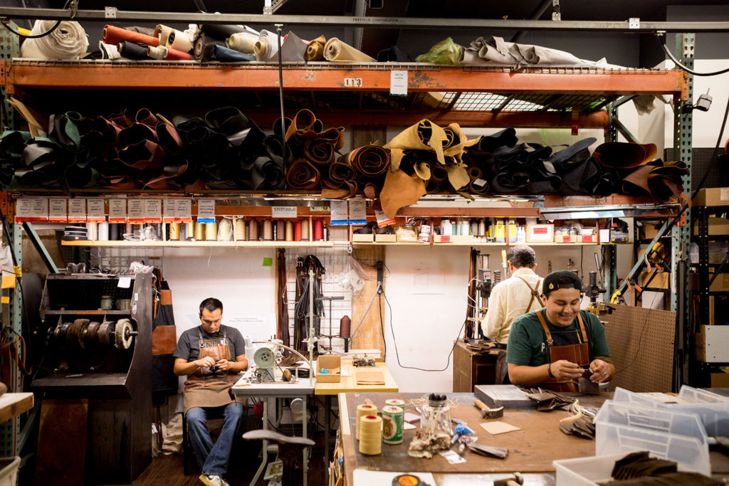 Three people working in a workshop surrounded by various tools and rolls of leather and fabric