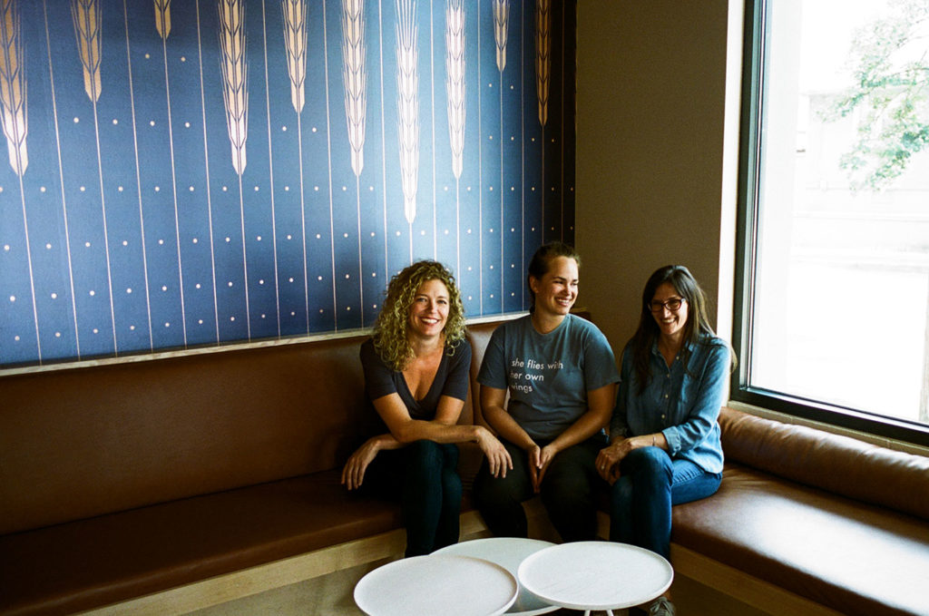 Three people sitting together on a bench inside of a building