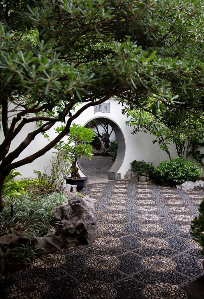 A courtyard with trees and a round archway in the background