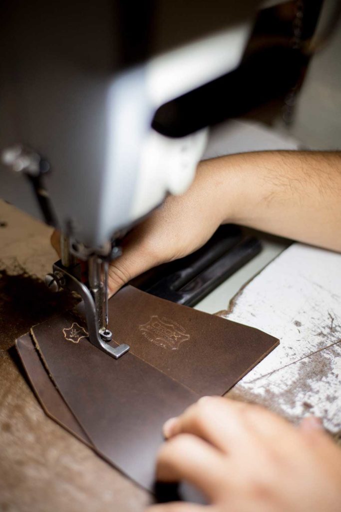 A person's hands sewing a piece of leather on a sewing machine