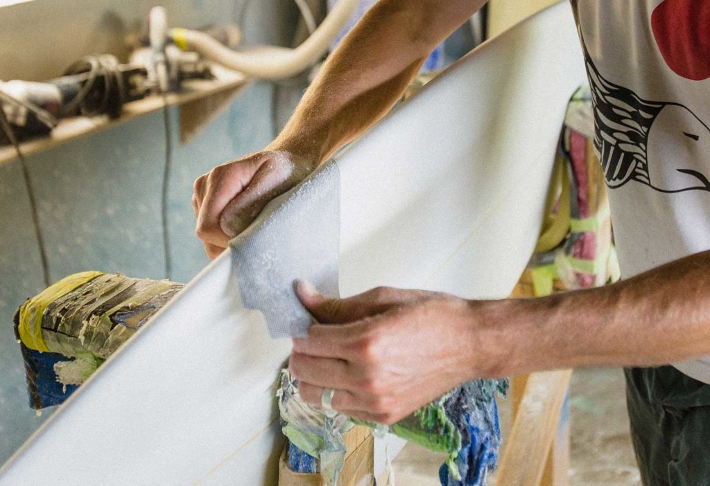 A person's hands sanding the edge of a surfboard