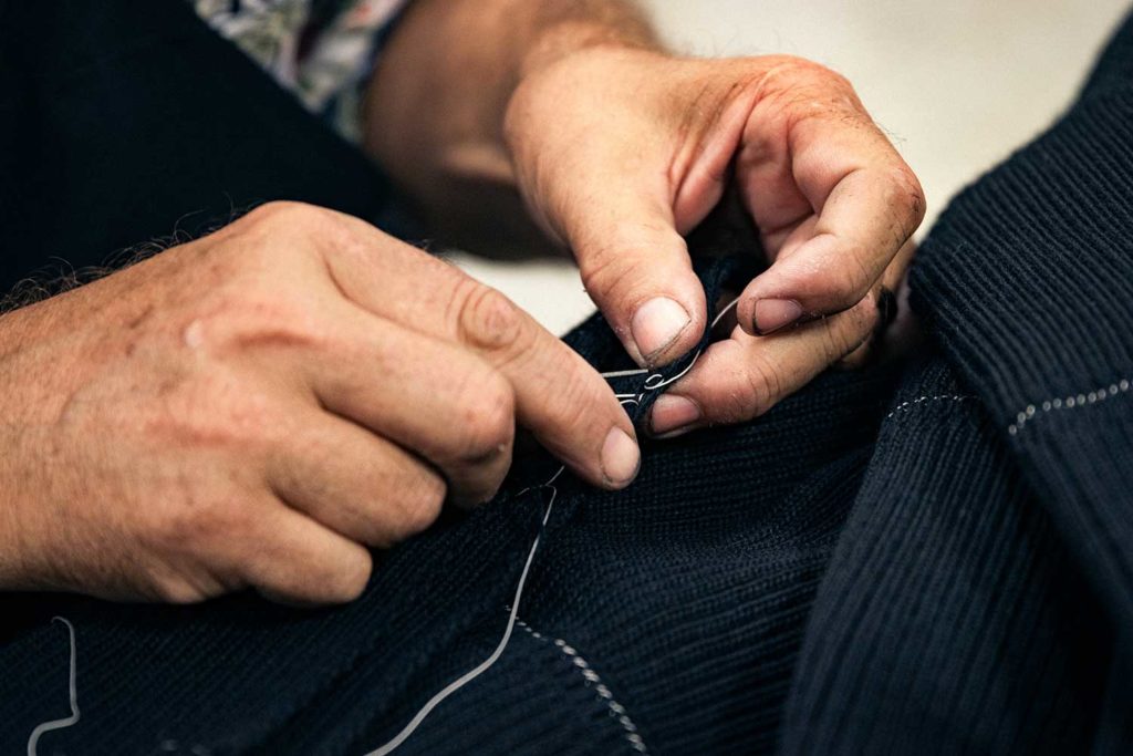 A close up of hands attaching a zipper to a piece of clothing