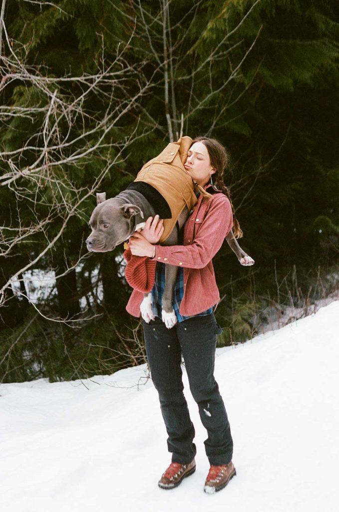 A woman carrying a dog in a snowy forrest