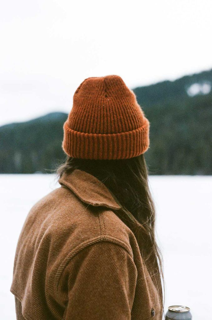 A person in an orange beanie looking out at a snow covered landscape
