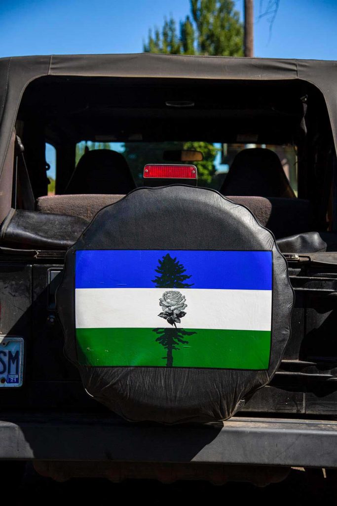 A spare tire cover with a blue, white, and green flag along with an image of a rose and pine tree