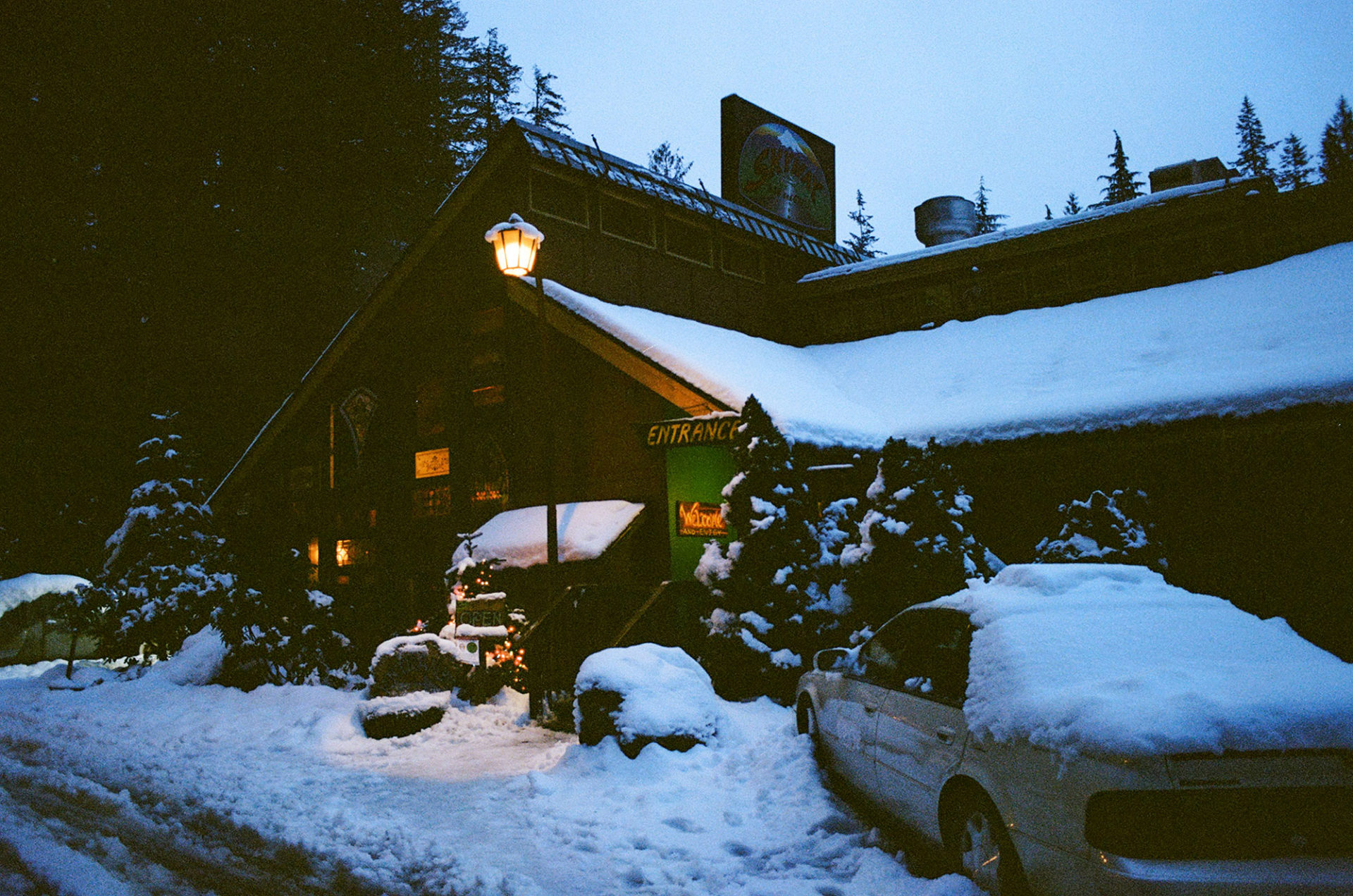 Cabin in the woods with a car out front covered by snow